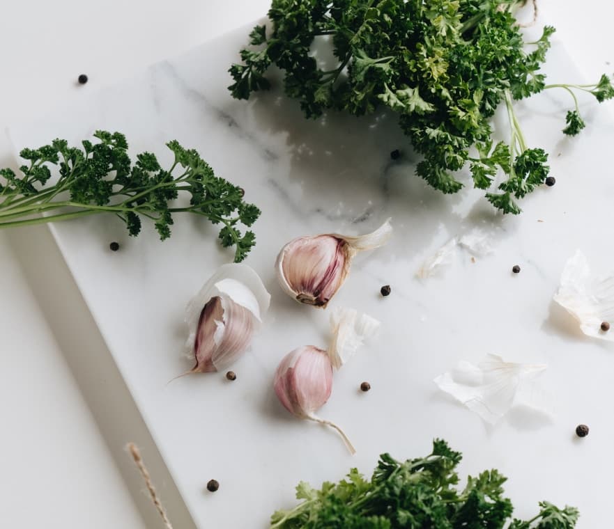 Knoblauch, Pfefferkörner und frische Petersilie auf einer Marmorplatte