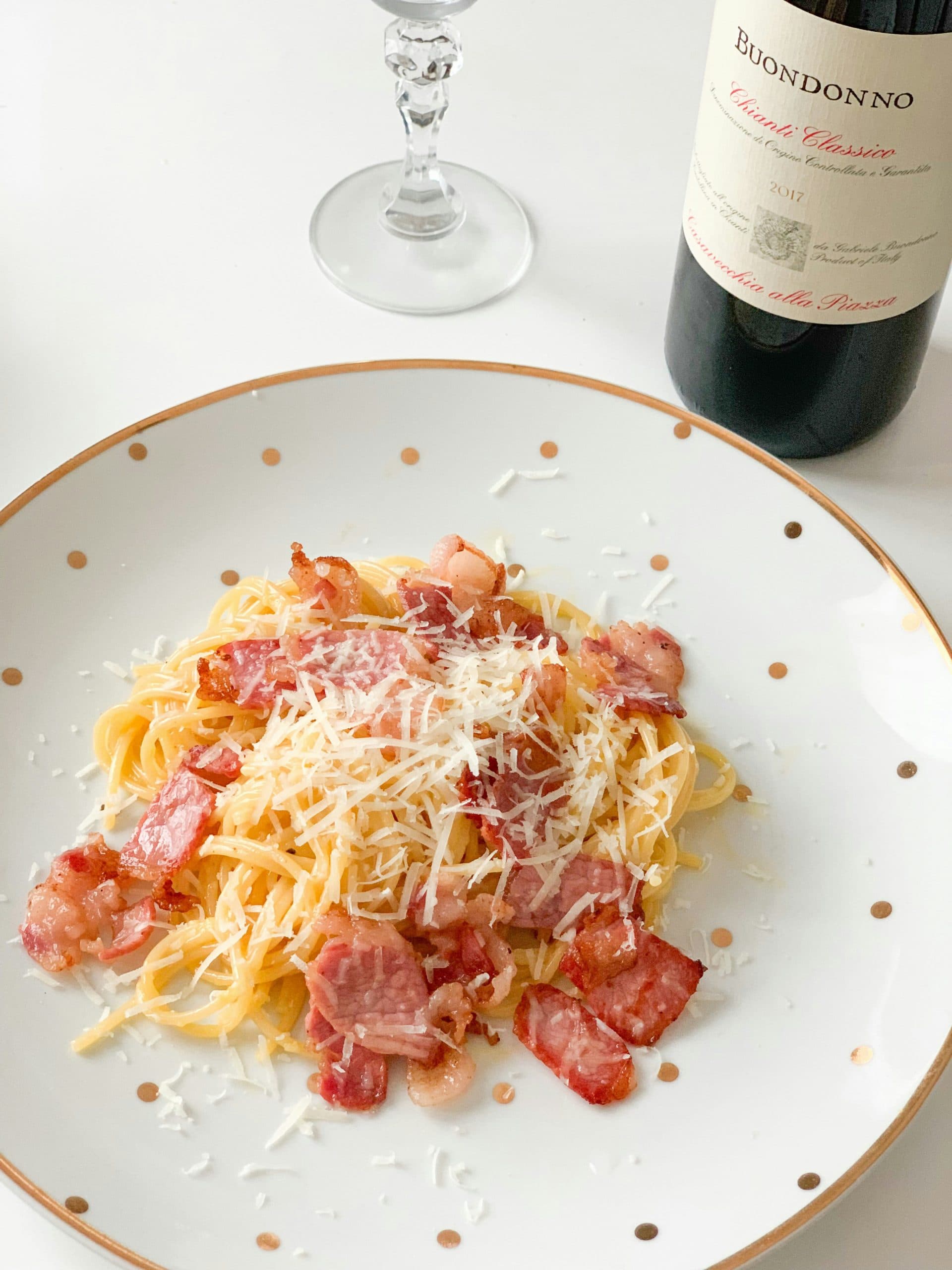 Teller Spaghetti Carbonara mit Speck und Parmesan neben einer Weinflasche